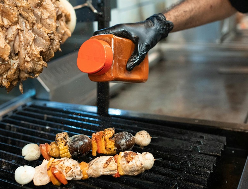 someone seasoning meat on a grill