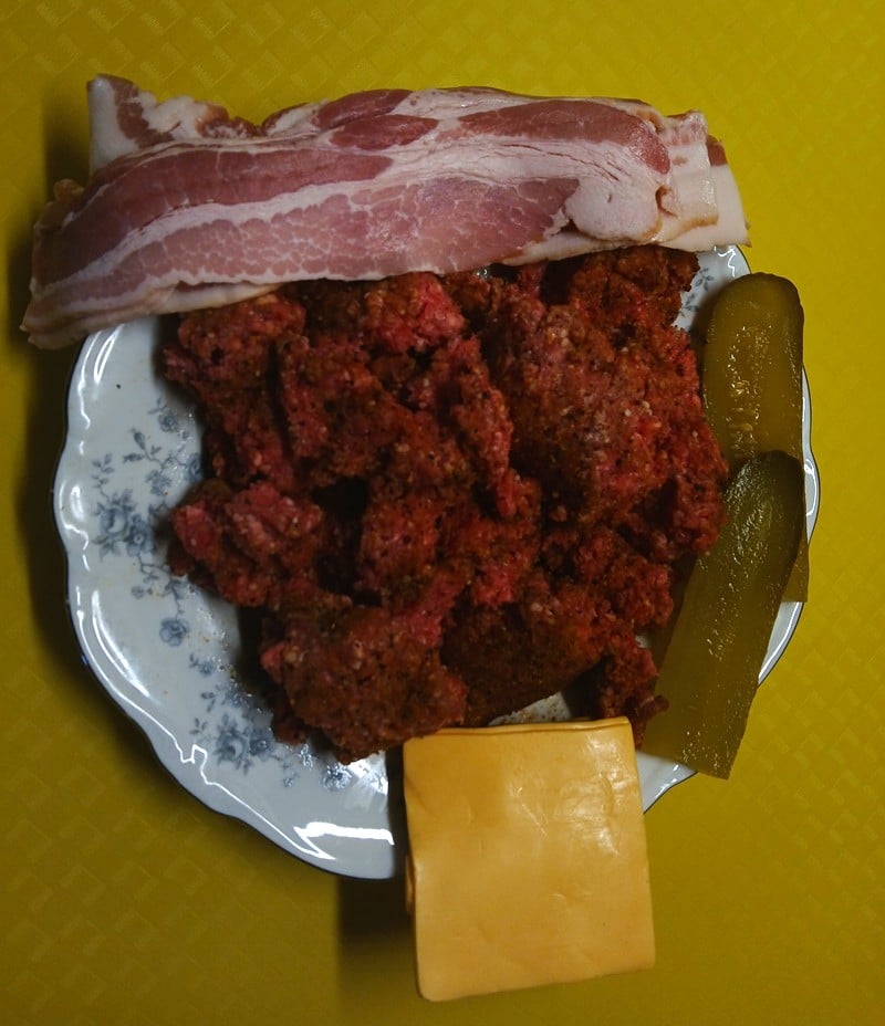 plate with  hamburger, bacon, pickle, and  cheese.