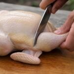 whole chicken being cut up in 8 pieces on a wooden cutting board