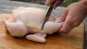 whole chicken being cut up in 8 pieces on a wooden cutting board